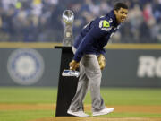 Seattle Seahawks quarterback Russell Wilson stands by the Vince Lombardi Trophy as he winds up to throw the ceremonial first pitch Tuesday at the Seattle Mariners' baseball home-opener.