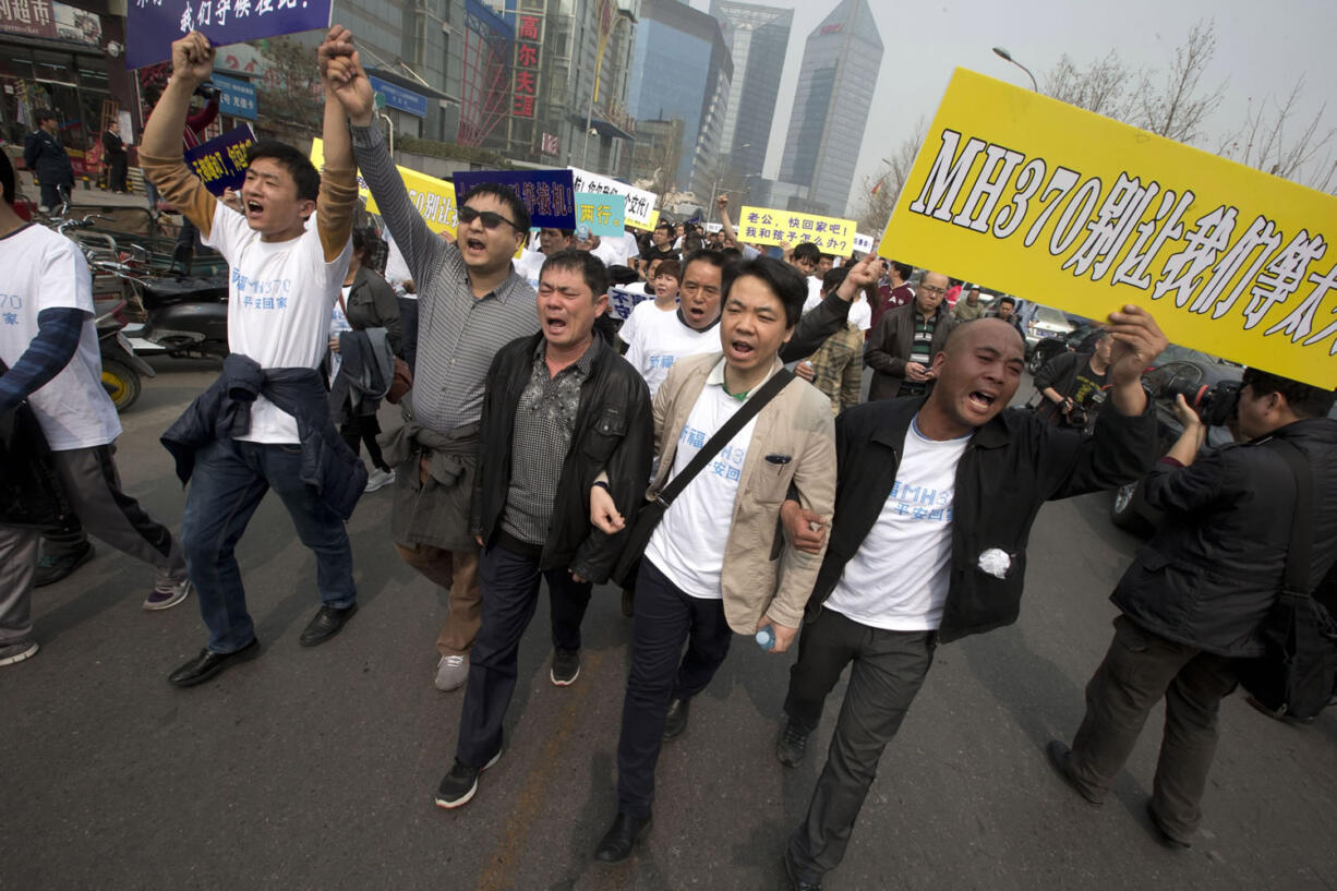 Relatives of Chinese passengers on a missing Malaysia Airlines plane protest with signs, one of which reads &quot;MH370, Don't let us wait too long&quot; as they march towards the Malaysian embassy Tuesday in Beijing.