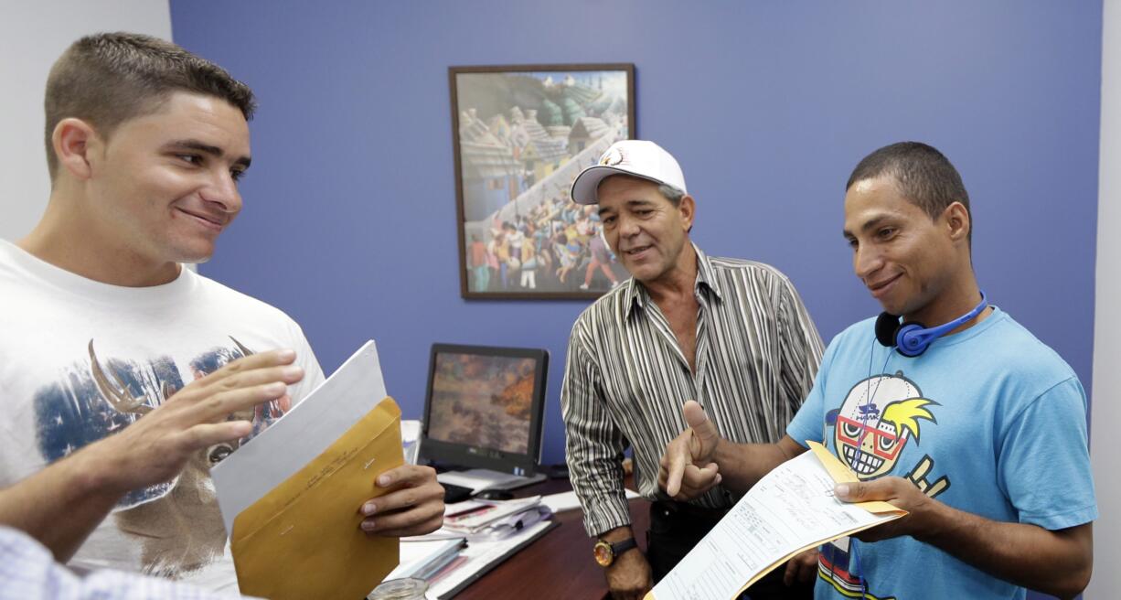 Jose Fuente Lastre, from left, Antonio Cardenas and Yennier Martinez Diaz open immigration documents Oct. 28 at the Church World Service office in Miami.