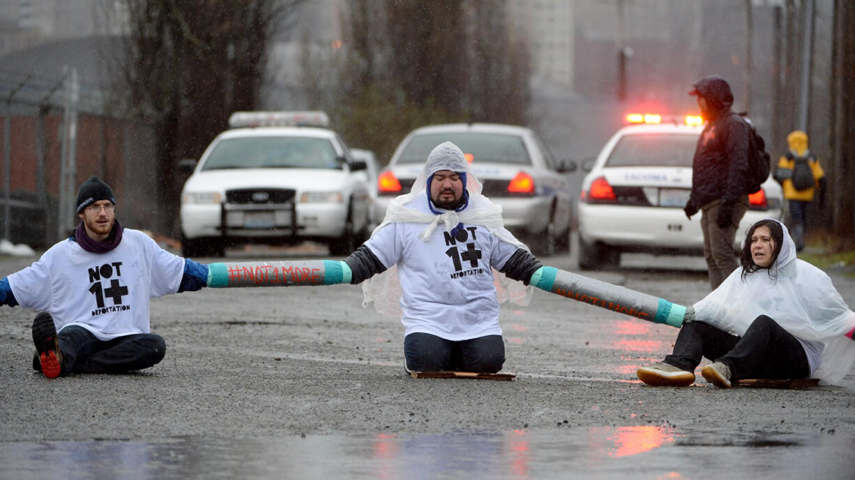 Protesters Joe Hiller, left, Milton Cornejo, center, and Maru Mola sit chained together blocking the road in front of the federal Northwest Detention Center in the Tacoma Tideflats on Monday.