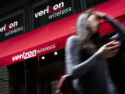 A pedestrian uses her cell phone as she passes a Verizon Wireless store on Broadway in Lower Manhattan in New York.