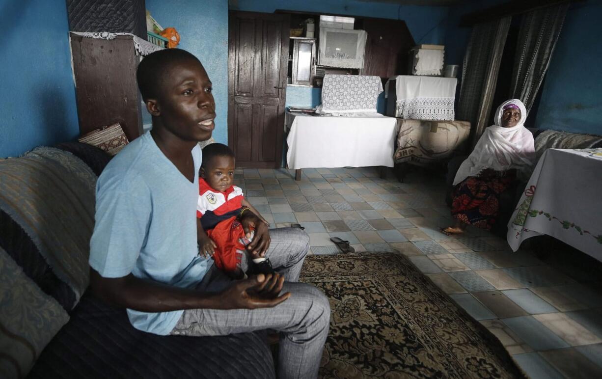 Nurse Donnell Tholley, 25, holds his adopted son Donnell Junior at their apartment  Aug. 18 in Freetown, Sierra Leone, as the baby's great-grandmother Marie looks on. Tholley adopted the boy following the death of the mother Fatu Turay last year from the Ebola virus at the hospital on the outskirts of Freetown, Sierra Leone.