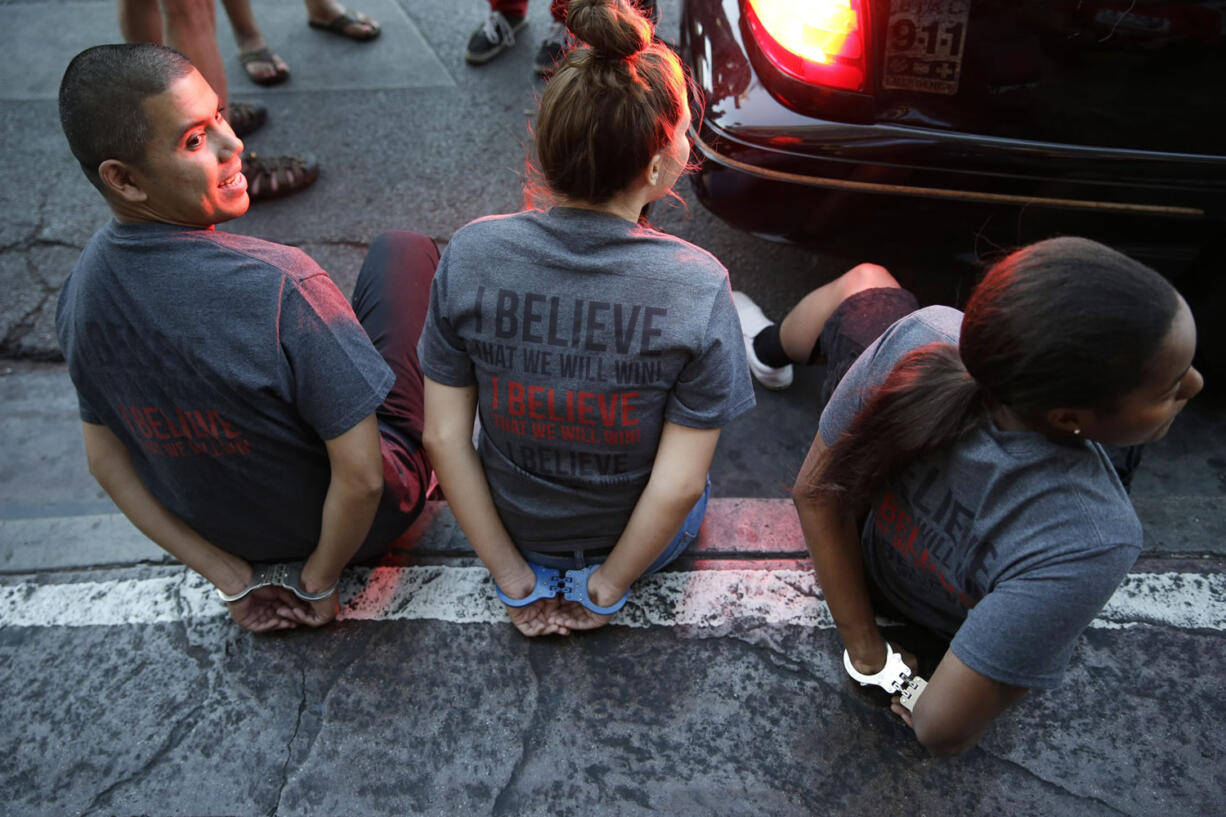 Handcuffed protestors sit on a curb Thursday in Las Vegas.