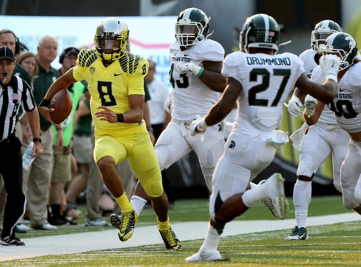 Oregon quarterback Marcus Mariota, left, runs down the sidelines ahead of a host of Michigan State defenders during the 3rd quarter of their NCAA college football game in Eugene, Oregon, Saturday Sept. 6, 2014.