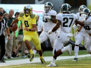 Oregon quarterback Marcus Mariota, left, runs down the sidelines ahead of a host of Michigan State defenders during the 3rd quarter of their NCAA college football game in Eugene, Oregon, Saturday Sept. 6, 2014.