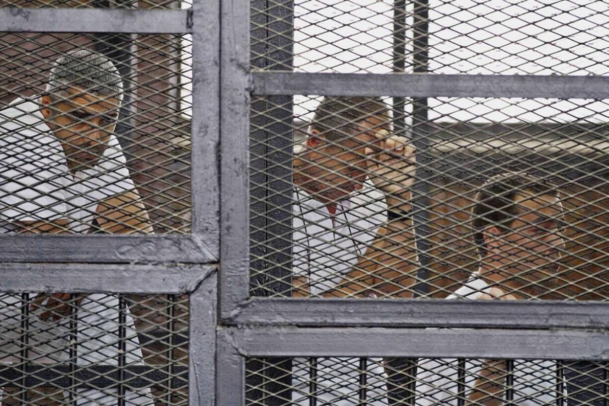 Mohammed Fahmy, from left, Canadian-Egyptian acting bureau chief of Al-Jazeera, Australian correspondent Peter Greste, and Egyptian producer Baher Mohamed appear in a defendantu2019s cage along with several other defendants during their trial on terror charges at a courtroom in Cairo.