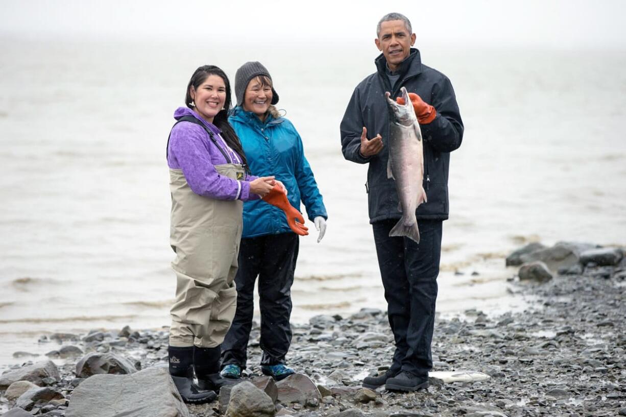 President Barack Obama holds up a fish while visiting with Commercial and Subsistence Fishers Alannah Hurley, left, and Kim Williams, center, on Kanakanak Beach, Wednesday, Sept. 2, 2015, in Dillingham, Alaska. Obama is on a historic three-day trip to Alaska aimed at showing solidarity with a state often overlooked by Washington, while using its glorious but changing landscape as an urgent call to action on climate change.