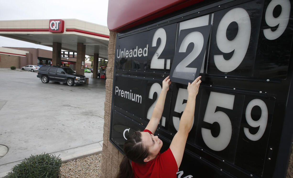 In this Friday, Dec. 12, 2014 photo, Quick Trip clerk Roxana Valverde adjusts the gas price sign numbers at a Tolleson, Ariz. QT convenience store as gas prices continue to tumble nationwide. The price of oil has fallen by nearly half in just six months, a surprising and steep plunge that has consumers cheering, producers howling and economists wringing their hands over whether this is a good or bad thing. (AP Photo/Ross D.