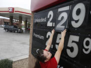 In this Friday, Dec. 12, 2014 photo, Quick Trip clerk Roxana Valverde adjusts the gas price sign numbers at a Tolleson, Ariz. QT convenience store as gas prices continue to tumble nationwide. The price of oil has fallen by nearly half in just six months, a surprising and steep plunge that has consumers cheering, producers howling and economists wringing their hands over whether this is a good or bad thing. (AP Photo/Ross D.