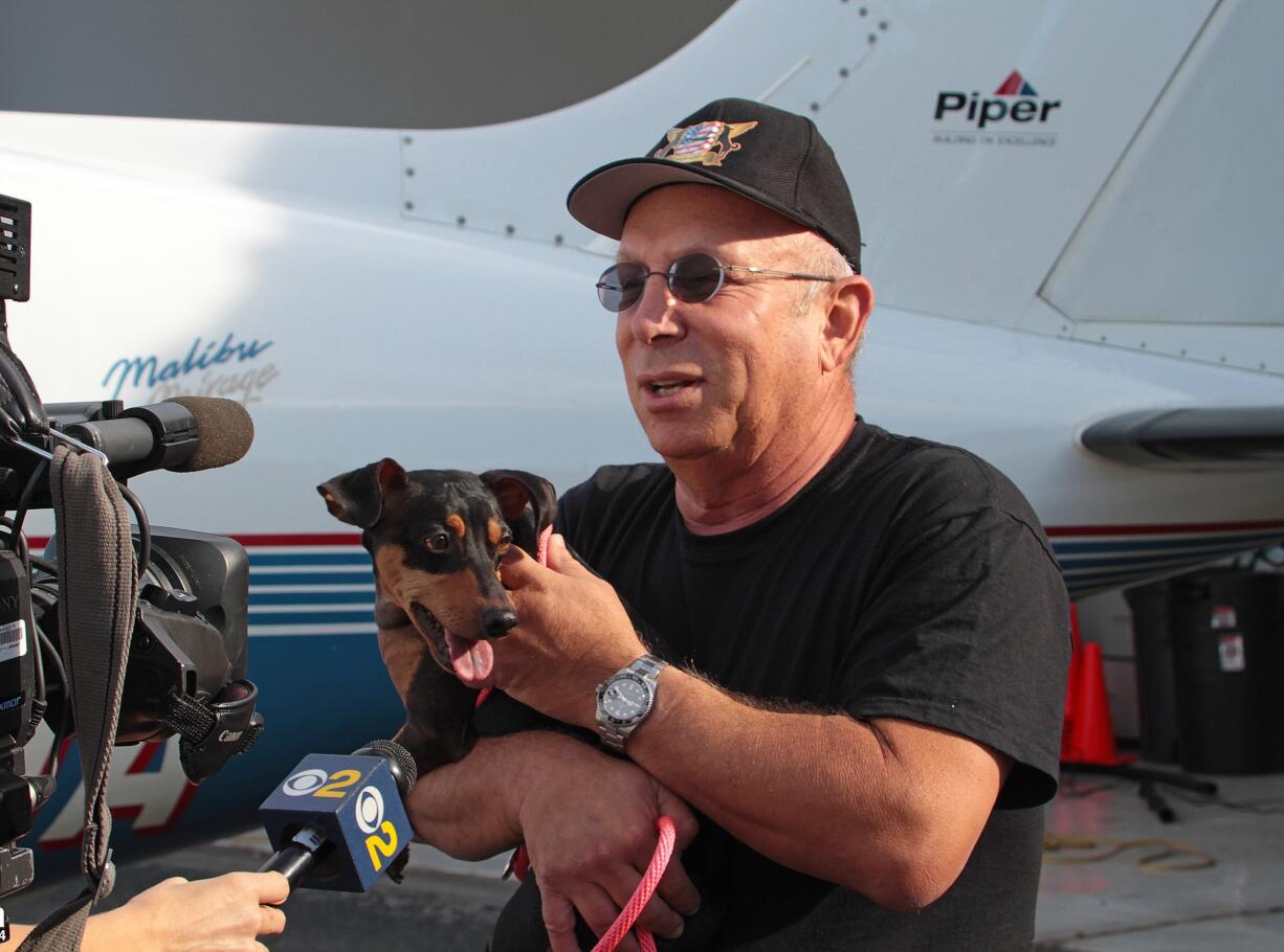 Yahuda Netanel, a private pilot with Wings of Rescue, holds a rescue dog as he stands by his plane prior to a flight at Van Nuys Airport, in Van Nuys, Calif.