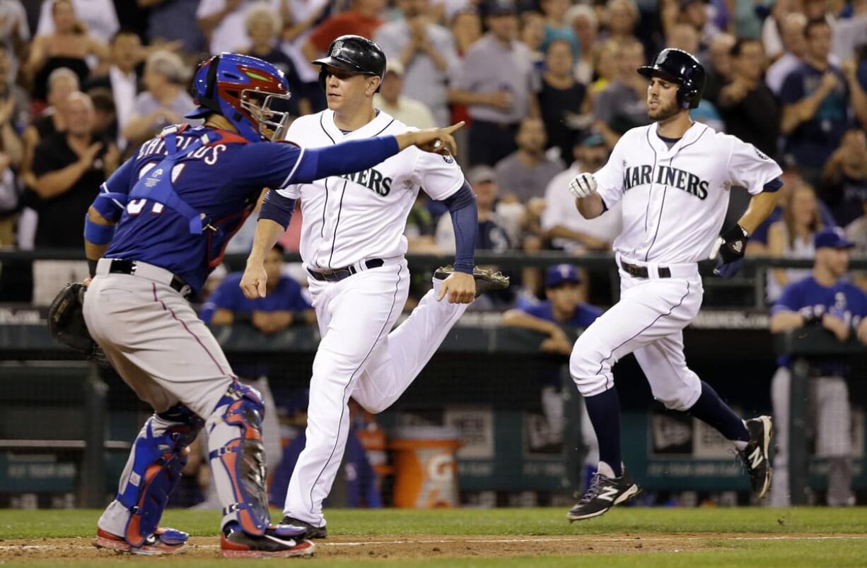 Seattle Mariners' Logan Morrison, center, is followed closely by Chris Taylor as the pair head home past Texas Rangers catcher Robinson Chirinos in the fourth inning of a baseball game Tuesday, Aug. 26, 2014, in Seattle.