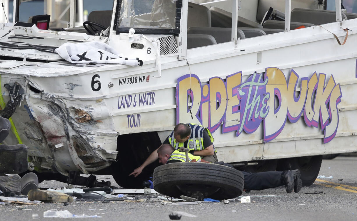 Seattle Police officers look under a &quot;Ride the Ducks&quot; tourist vehicle as a tire and wheel from the bus sits nearby before the bus is loaded onto a flatbed tow truck Thursday, after it was involved in a fatal crash with a charter passenger bus earlier in the day in Seattle. (Ted S.