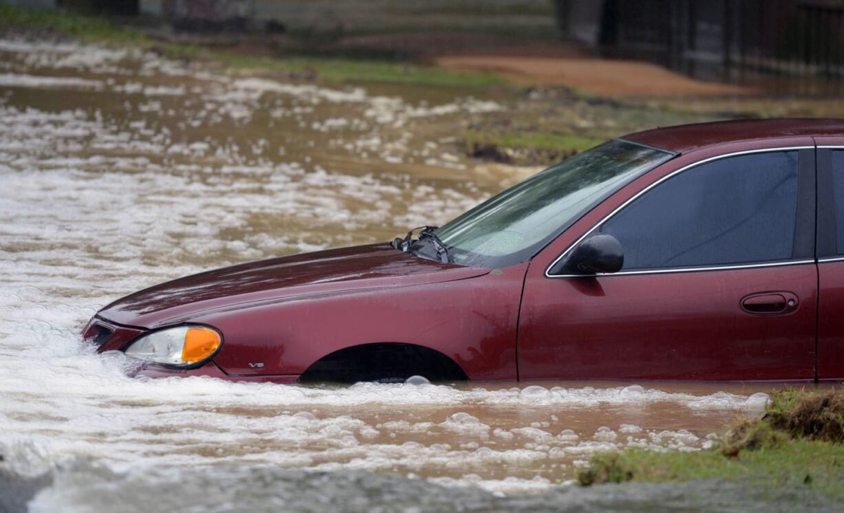 A vehicle, surrounded waters up to the tops of its tires, sits abandoned in Beulah, Fla., on a flooded stretch of Mobile Highway following heavy rains near Pensacola, Fla., on Wednesday.