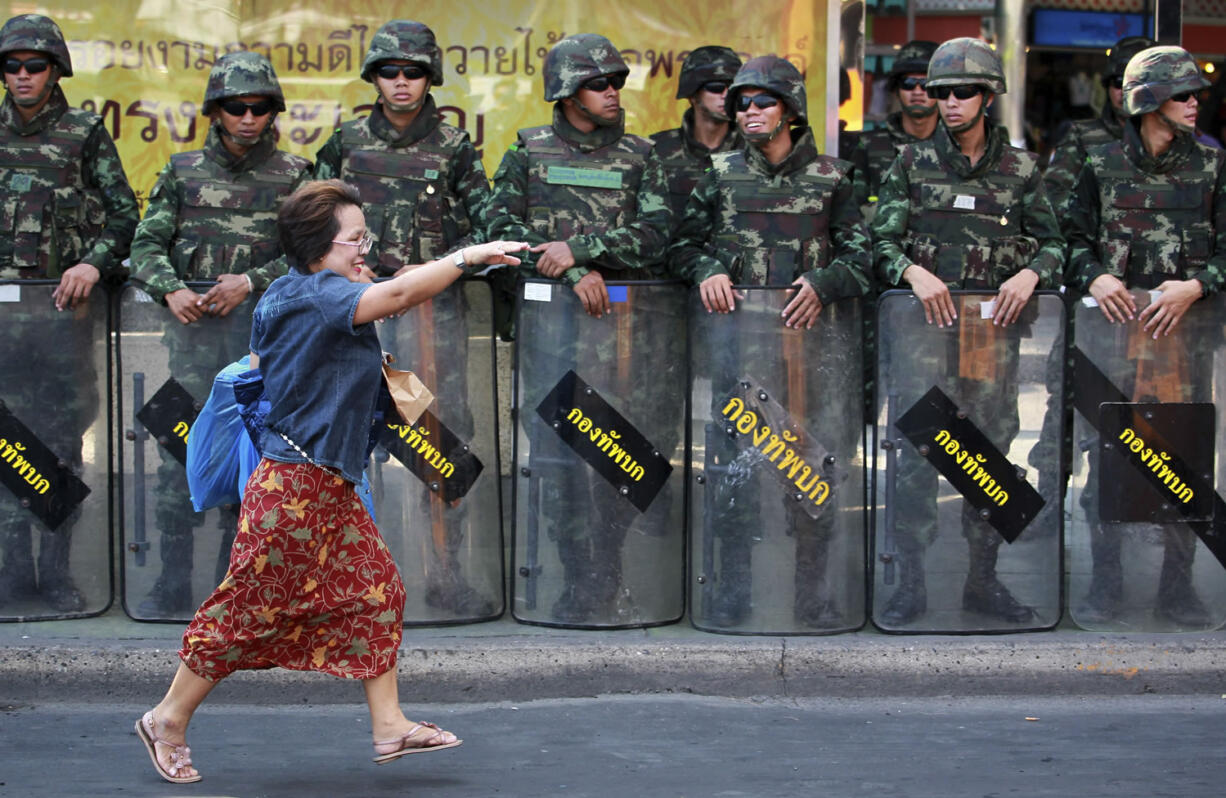 A woman runs for a waiting vehicle Friday past line of Thai soldiers guarding the square at Victory Monument to prevent anti-coup demonstration in Bangkok, Thailand.