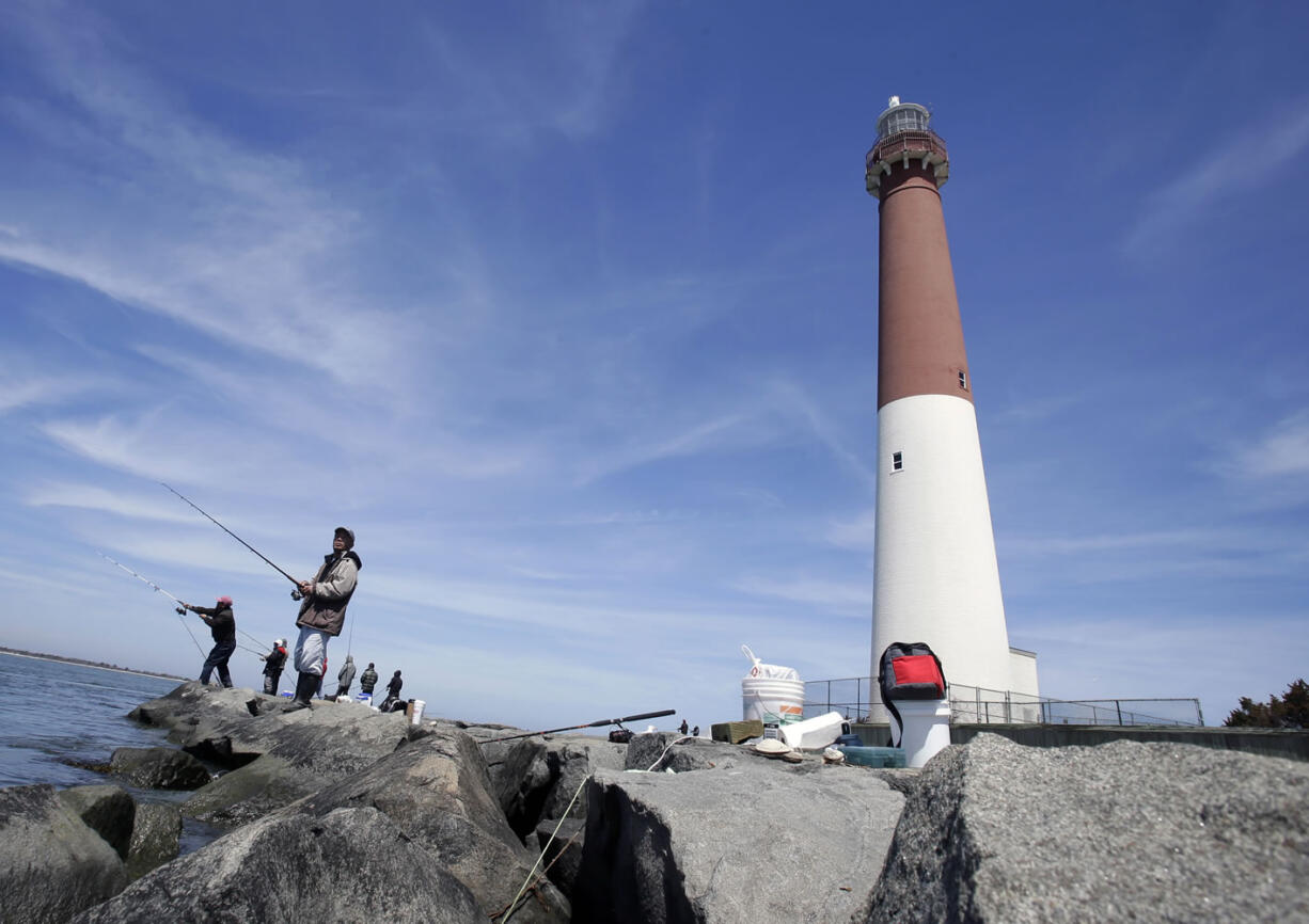 FILE - This April 30, 2013 file photo shows people fishing near the Barnegat Lighthouse on Long Beach Island, N.J. The Jersey shore is full of spots to drop a baited line or a wire trap over the side of a bulkhead, and come up with a bucket full of tasty blue claw crabs. Theyire biting now and will be through the end of September. And the beaches and jetties are prime surf-fishing spots after the lifeguards pack up and leave in the evenings.