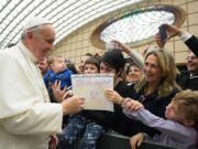 In this picture made available by the Vatican newspaper L' Osservatore Romano, Pope Francis is presented by a child with a drawing depicting a Pope's portrait and a writing which reads Merry Christmas, during an audience with the Holy See's employees in the Paul VI hall at the Vatican, Monday, Dec. 22, 2014.