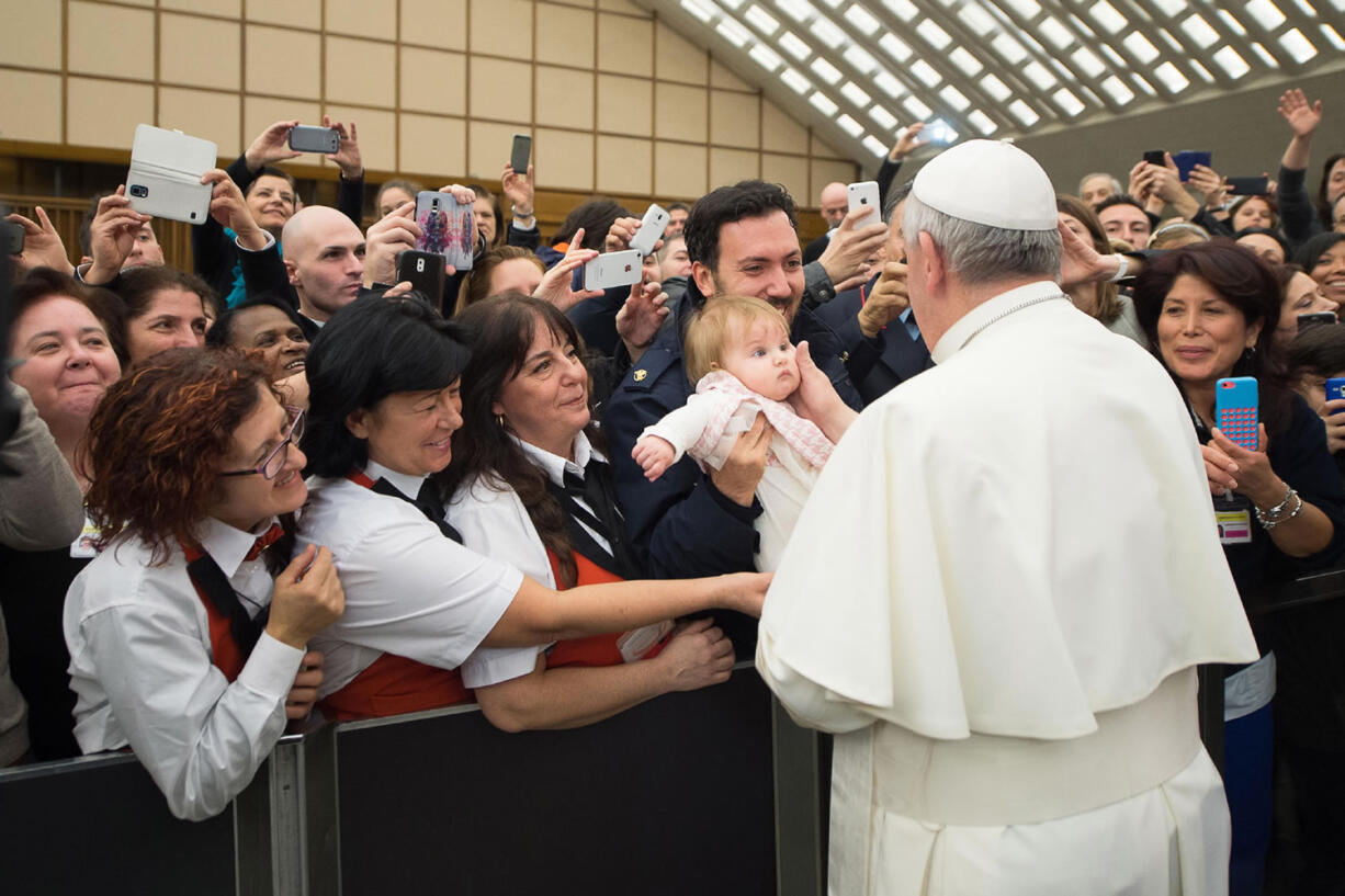 Pope Francis caresses a baby as he greets faithful during an audience with the Holy See's employees in the Paul VI hall at the Vatican on Monday.