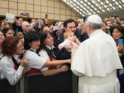 Pope Francis caresses a baby as he greets faithful during an audience with the Holy See's employees in the Paul VI hall at the Vatican on Monday.