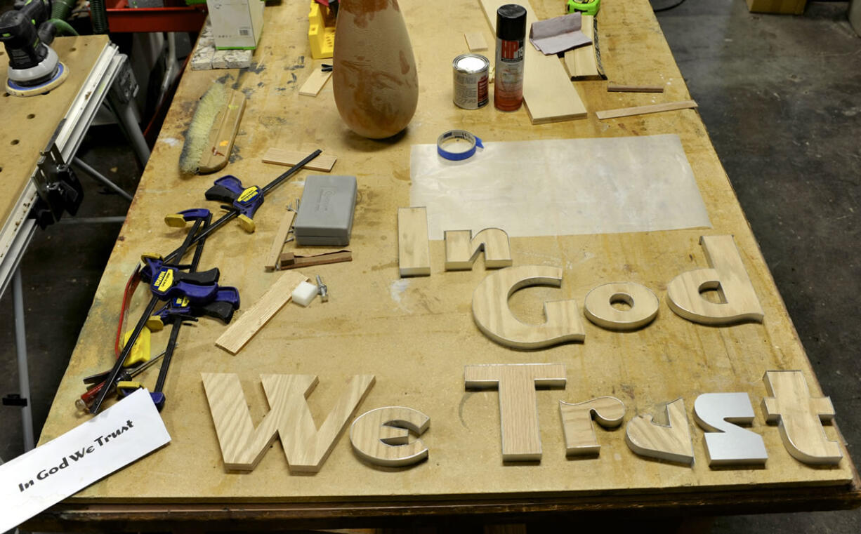 Wooden letters laid out on a work bench at the Friends of the Carpenter will soon spell out "In God We Trust" in the Clark County council's hearings room.