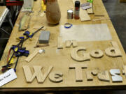 Wooden letters laid out on a work bench at the Friends of the Carpenter will soon spell out "In God We Trust" in the Clark County council's hearings room.