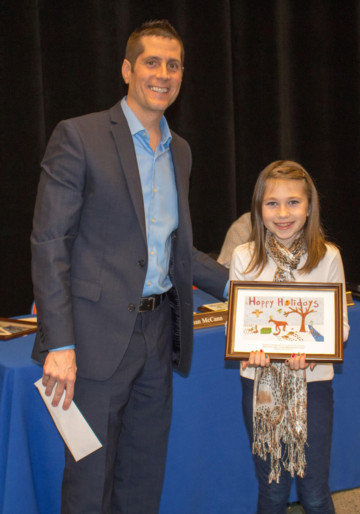 Ridgefield: Ridgefield School District Superintendent Nathan McCann congratulates Union Ridge Elementary School student Olivia Fenton on winning the Holiday Greeting Card Design Competition at a district board meeting on Dec.