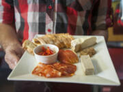 A server holds a Paysan Plate, which includes seasonal crostini, pate, vegetables, french cheese and warm baguette.