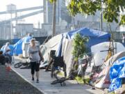 A woman walks Wednesday past a homeless encampment of tents and huts on West 12th Street along a fence bordering the Port of Vancouver.