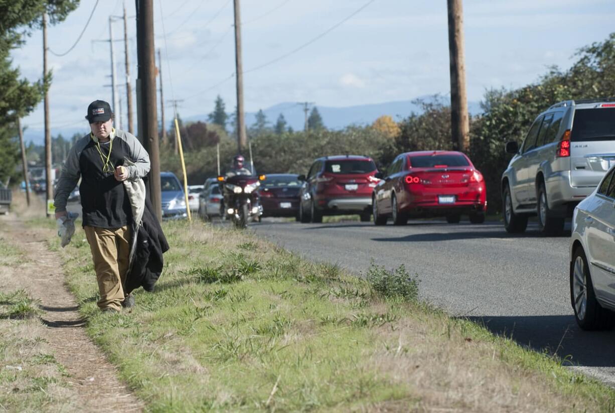 Heavy traffic whizzes by a pedestrian walking Tuesday on the shoulder of Southeast First Street in east Vancouver. The busy two-lane road eventually will get sidewalks, bike lanes, streetlights and stormwater drainage, but for now, the city lacks the money for the $16.3 million project.