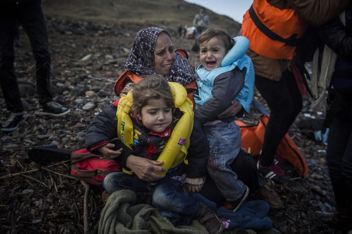 A woman holds two children on a beach Sunday after arriving on a dinghy from a Turkish coast to the northeastern Greek island of Lesbos.