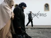 Muslim residents walk past racial slurs painted on the walls of a mosque in the town of Saint-Etienne, central France.