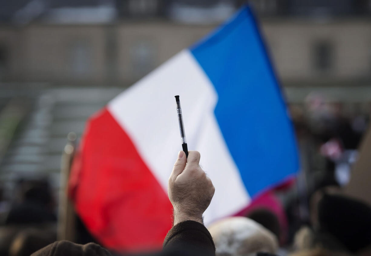 A demonstrator holds up a pen in front of the French flag as hundreds of people rally in support of free speech and to remember the victims of the recent terrorist attacks in France on Sunday in Toronto.