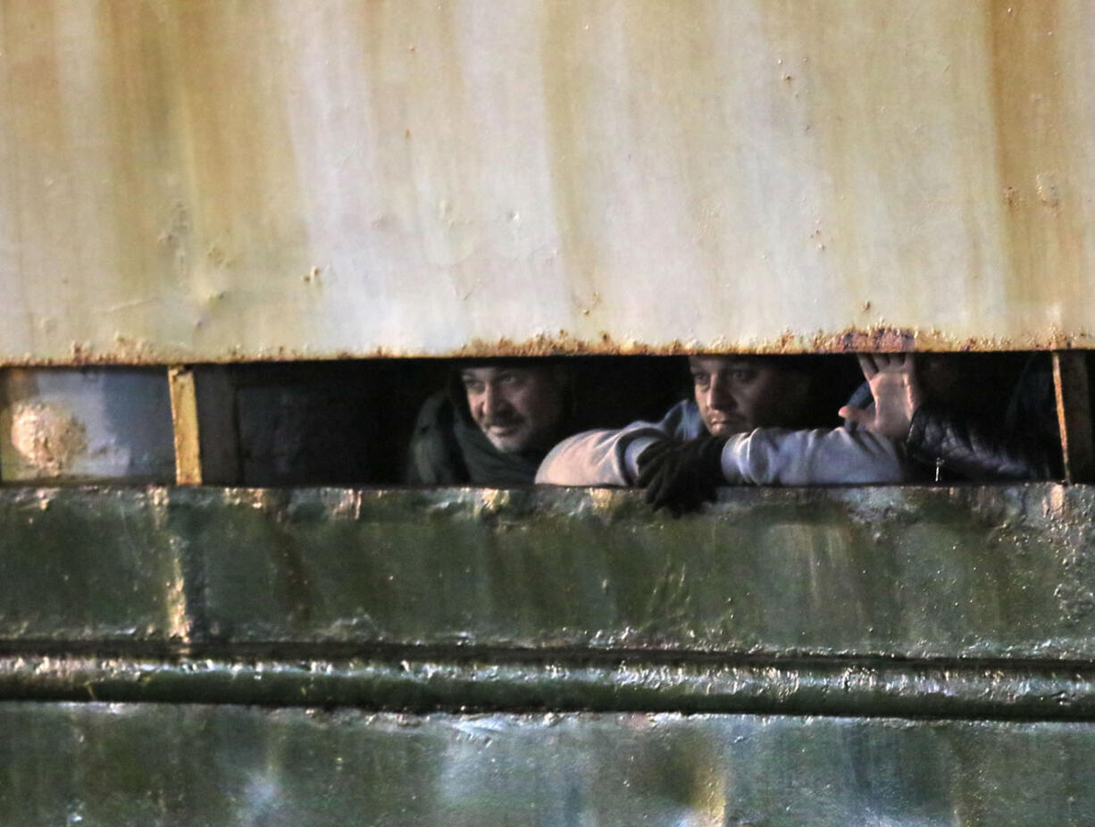 Men wait on board as the cargo ship Ezadeen, carrying hundreds of migrants, arrives at the southern Italian port of Corigliano, Italy, Saturday, Jan. 3, 2015. The cargo ship was stopped with about 450 migrants aboard after smugglers sent it speeding toward the coast in rough seas with no one in command. Italian authorities lowered engineers and electricians onto the wave-tossed ship by helicopter to secure it, and the Icelandic Coast Guard towed it to the Italian port of Corigliano late Friday night. Smugglers who bring migrants to Europe by sea appear to have adopted a new, more dangerous tactic: cramming hundreds of them onto a large cargo ship, setting it on an automated course to crash into the coast, and then abandoning the helm.