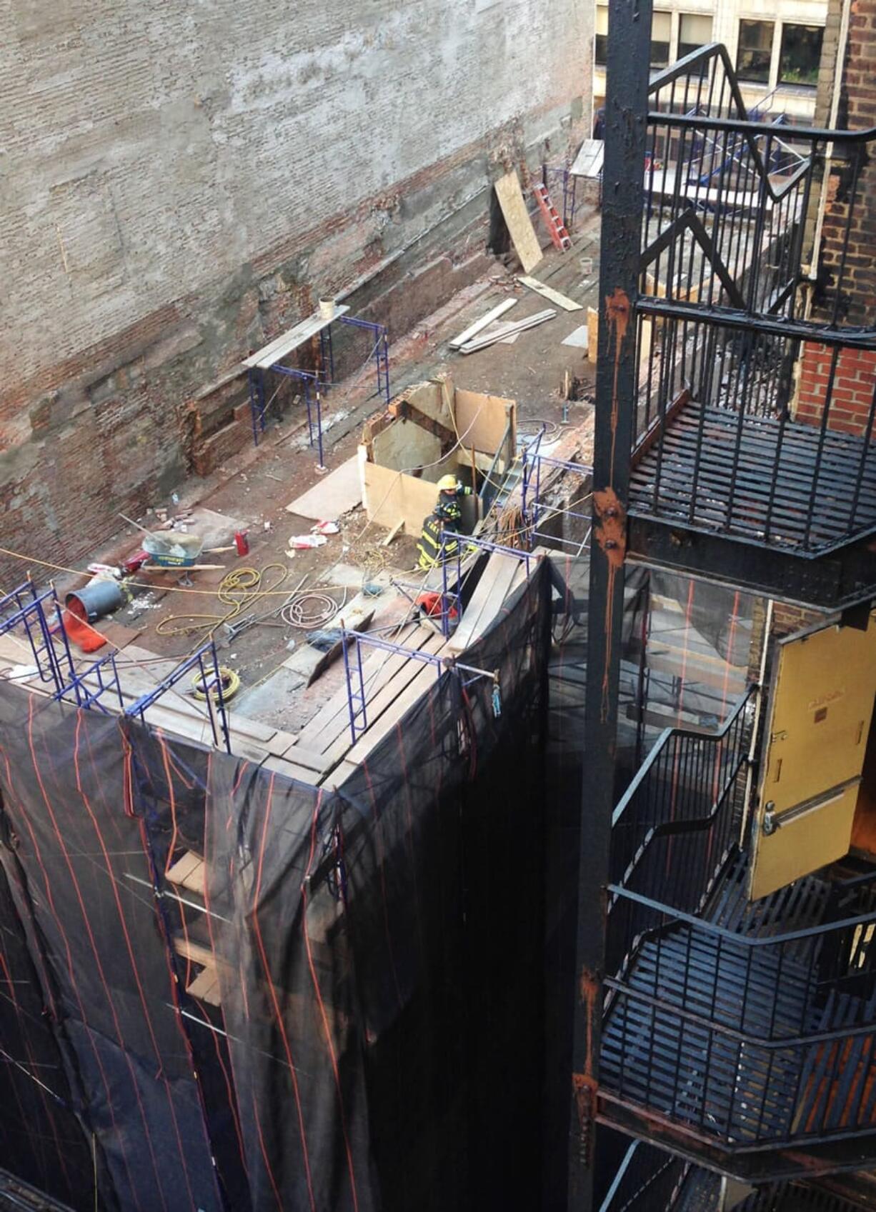 Firefighters on the top floor of a midtown Manhattan building look at a collapsed section of the building Friday in New York. One construction worker was killed and at least one other is trapped in the rubble, officials said. The building is being demolished to make way for a luxury boutique hotel.