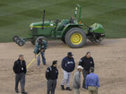 Seattle Mariners manager Lloyd McClendon, bottom center, talks with umpires Jim Reynolds (77) and Fieldin Culbreth (25) as members of the grounds crew work on the infield before a baseball game between the Mariners and the Oakland Athletics was postponed for unplayable field conditions.