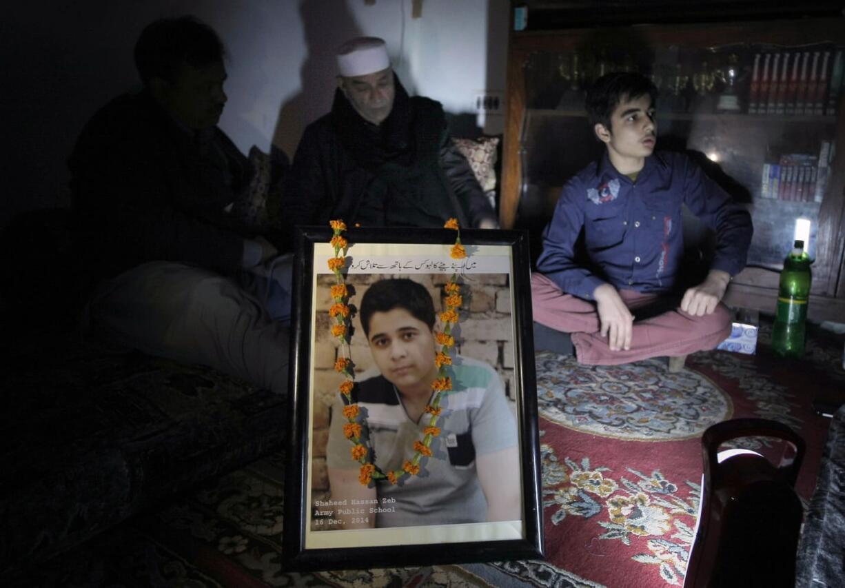 Aurangzeb Khan, center, and son Musa Zeb, right, speak next to the portrait of Hassan Zeb, who was killed in a  school attack, during an interview with The Associated Press in Peshawar, Pakistan.