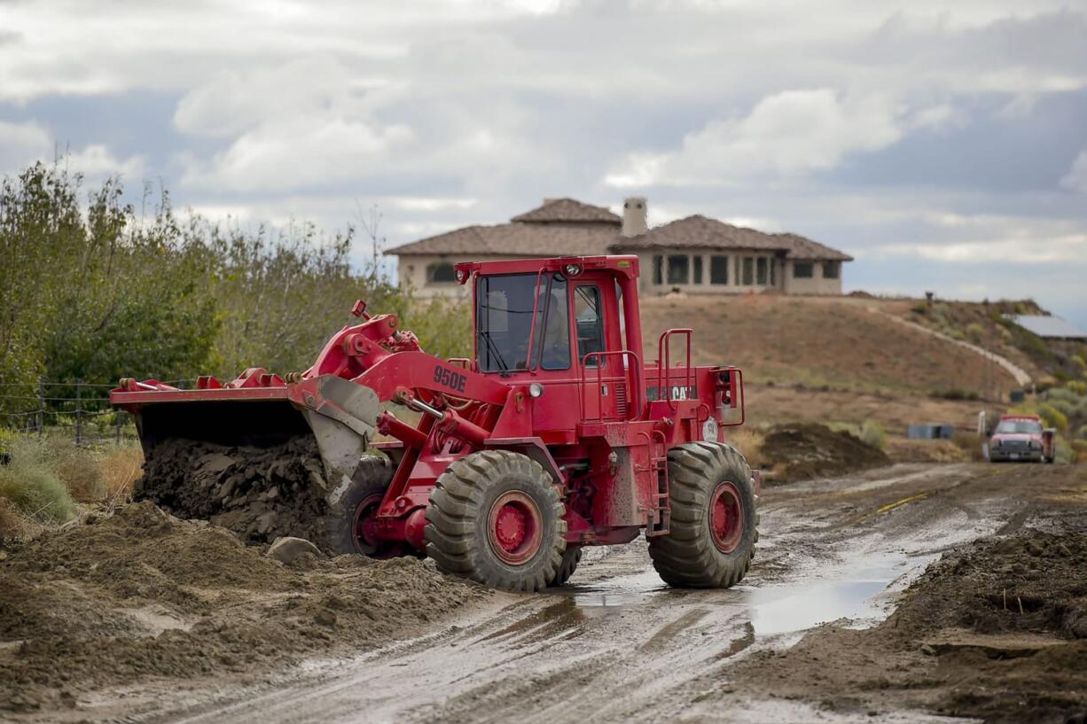 A Los Angeles County firefighter use a front end loader to clear mud on Friday after a flash floods the day before sent mud and debris through Elizabeth Lake road in Leona Valley, Calif., trapping cars and closing roads.