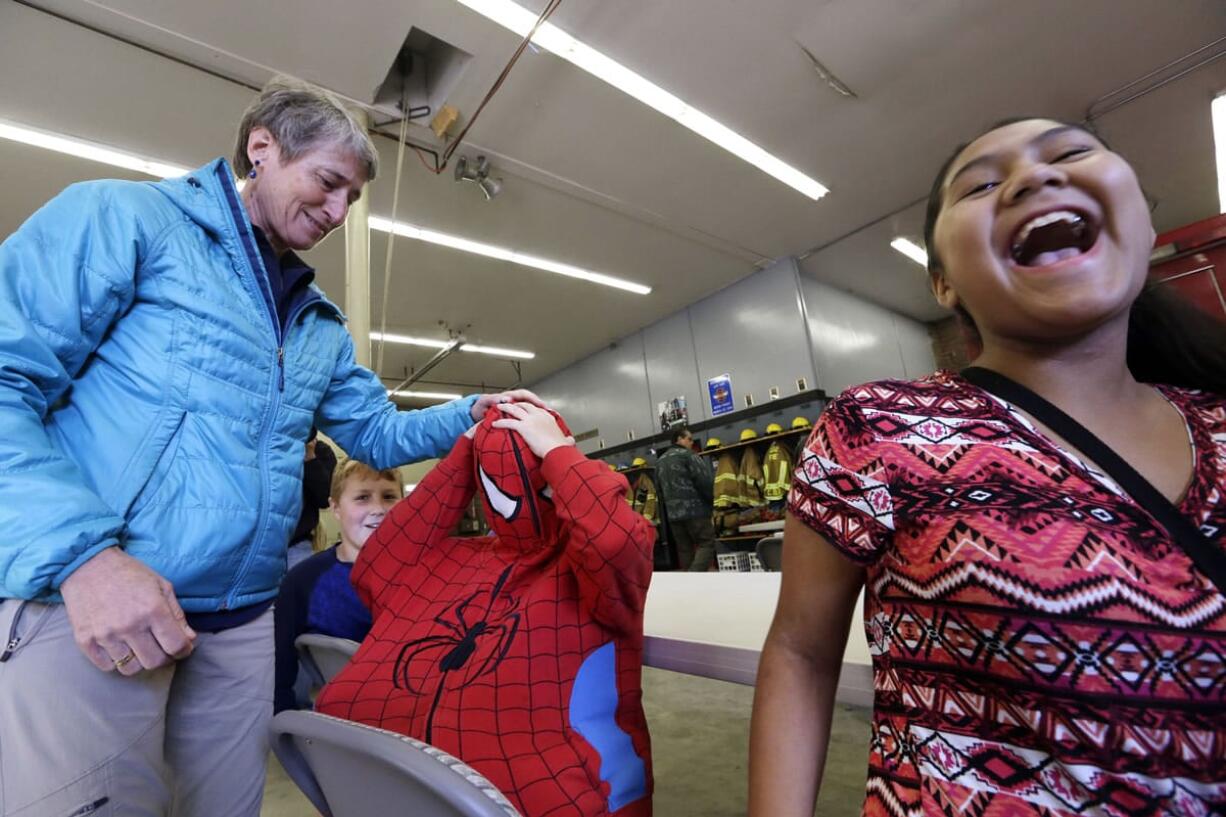 Sixth grader Jade Decoteau, right, lets out a laugh as Secretary of the Interior Sally Jewell, left, zips up the Spiderman sweatshirt of Nicholas Mankins into its full costume before an earthquake drill as part of a statewide Great ShakeOut drill at the Oso Firehouse Thursday in Oso.