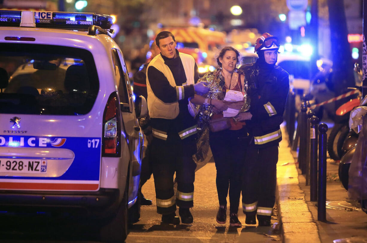 Rescue workers help a woman Friday outside the Bataclan theater in Paris, one of several sites around the city in a wave of attacks that prompted President Francois Hollande to announce he was closing the country&#039;s borders and declaring a state of emergency.