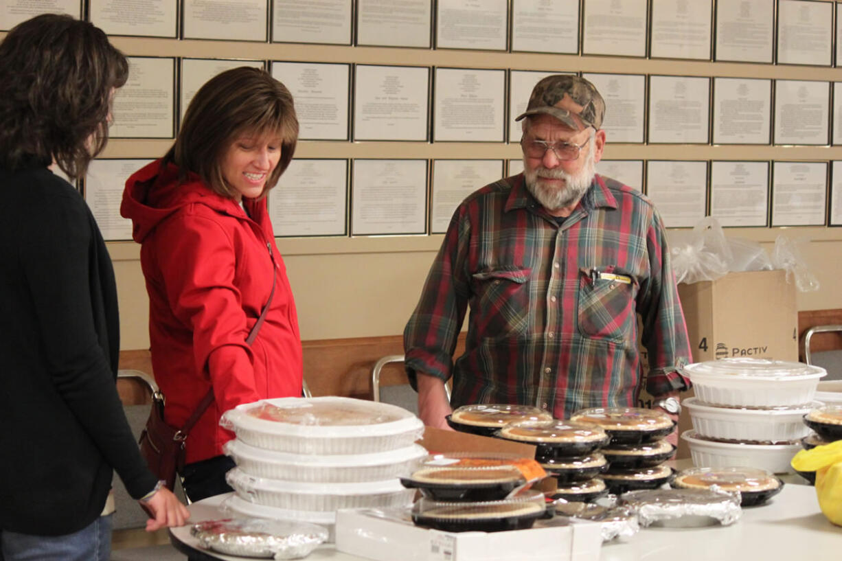 Volunteers Lora Rollins (center) and her daughter, Isabella, 12, talk to Al Schmid, who leads the annual coordination of the Knights of Columbus Thanksgiving dinner preparation and delivery. Schmid, 75, has been participating in the effort for 29 years. &quot;He is very humble,&quot; Lora Rollins said of Schmid. &quot;He does so much. He is always there to lend a hand if you need it.