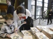 Melissa Carroll, a digital technology student at Washington State University Vancouver, and her son, Liam Carroll, 4, pick up a book at the 2014 launch of the #nextchapter program at Vancouver City Hall.