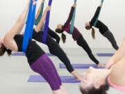 Women participating in an aerial yoga class stretch with the aid of silk hammocks.