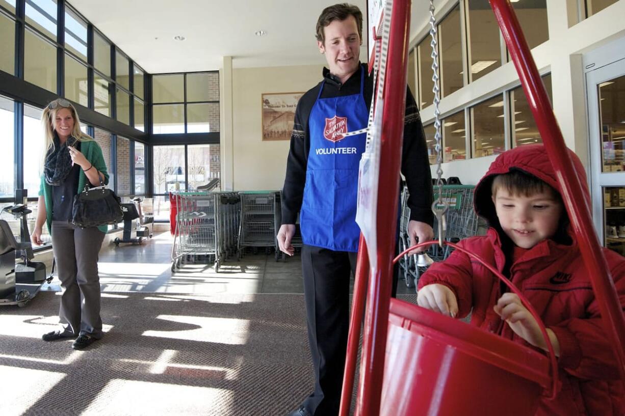 Spencer Bybee, 4, of Vancouver drops coins into a collection kettle on Thursday as Vancouver Mayor Tim Leavitt, center, and Spencer's mom, Chelsea Bybee, left, watch at the Grand Central Fred Meyer.