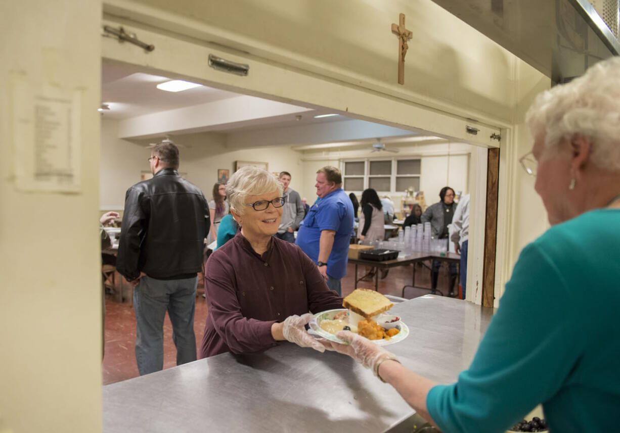 Volunteer waitress Mary Beth Sokolik, center, collects a plate from fellow volunteer Dorothy Marks before walking it out to a dinner guest at the Proto-Cathedral of St. James the Greater on Thanksgiving Day in Vancouver. Over Sokolik&#039;s left shoulder in a blue T-shirt is Mike Sortors, a volunteer who oversees the whole program. Dignity is the point, Sortors said, which is why guests are waited on like restaurant patrons. The meals were among several served by different churches and organizations Thursday in Clark County.