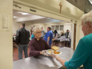 Volunteer waitress Mary Beth Sokolik, center, collects a plate from fellow volunteer Dorothy Marks before walking it out to a dinner guest at the Proto-Cathedral of St. James the Greater on Thanksgiving Day in Vancouver. Over Sokolik&#039;s left shoulder in a blue T-shirt is Mike Sortors, a volunteer who oversees the whole program. Dignity is the point, Sortors said, which is why guests are waited on like restaurant patrons. The meals were among several served by different churches and organizations Thursday in Clark County.