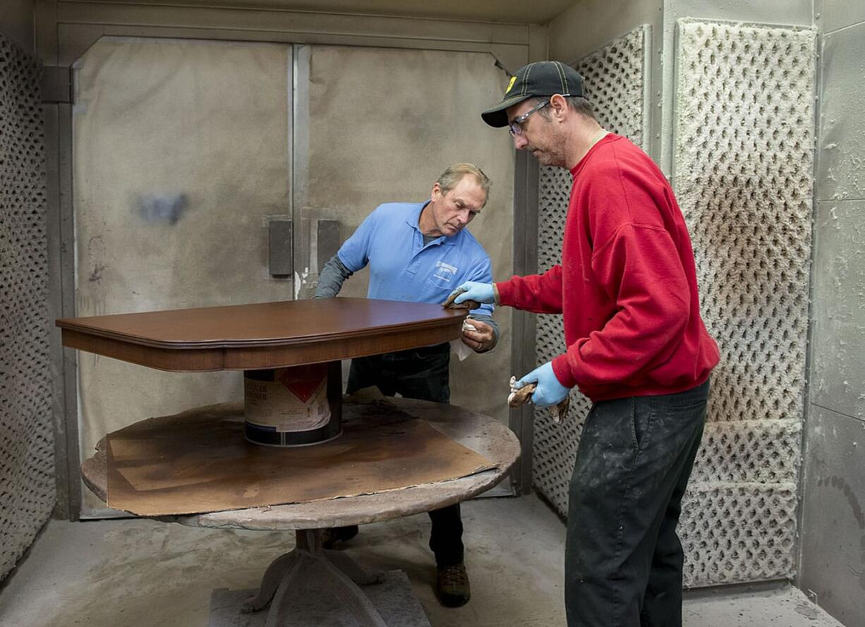 John Klumph, owner of Old Friends Furniture Finishing, center, stains a dining room table with Richard McKee in northeast Vancouver on Nov. 16.