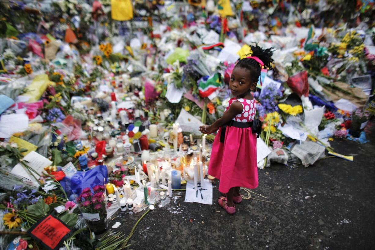 Four years old Bokamoso warms her hands over candles placed between flowers outside of the house of former South African President Nelson Mandela in Johannesburg, Monday, Dec. 9, 2013. Scores of heads of state and government and other foreign dignitaries, including royalty, are beginning to converge on South Africa as the final preparations for Tuesday's national memorial service for liberation struggle icon Nelson Mandela are put in place.