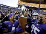 Washington players, including Jaydon Mickens, left, and Brian Clay, center, cheer as they hold the Apple Cup trophy after the team beat Washington State in an NCAA college football game Friday, Nov. 27, 2015, in Seattle. Washington won the annual Apple Cup game, 45-10.