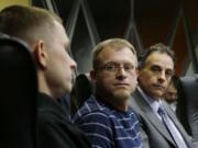 Eli Hall, center, looks on as his husband, Michael Hall, left, talks to reporters Tuesday  in Seattle.