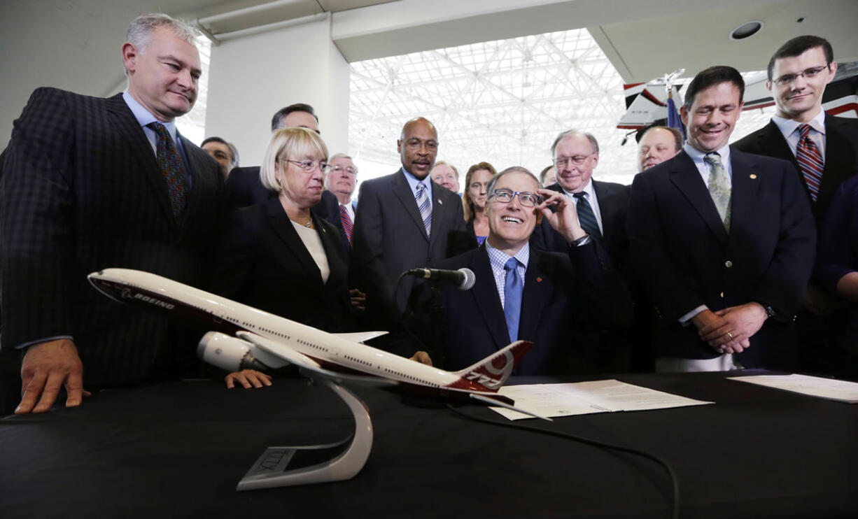 Gov. Jay Inslee, center, adjusts his glasses as he prepares to sign legislation to help keep production of Boeing's new 777X in Washington on Monday at the Museum of Flight in Seattle.