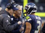 Seattle Seahawks quarterback Russell Wilson (3) talks with head coach Pete Carroll, center, and offensive coordinator Darrell Bevell before Wilson's final play against the Tampa Bay Buccaneers in overtime in an NFL football game Sunday, Nov. 3, 2013, in Seattle. The Seahawks won 27-24 on a field goal in overtime.